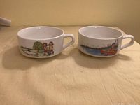 Two white handled soup bowls side by side displaying different Campbell’s Soup Kids graphics