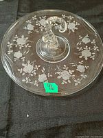 Top view of clear glass serving plate showing etched floral pattern, scalloped edge and central handle