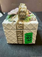 Side view of Fitz and Floyd ceramic trinket box showing basket-weave texture, ribbon detail and lot sticker