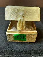figurine inside cream presentation box, lid partially closed showing tassel