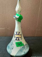 Side view of porcelain decanter showing stopper, scenic design and label