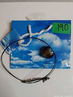 Necklace coiled showing multi strands, clasp, and heart pendant alongside gift bag with lot tag