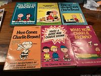 Front covers of all six Peanuts cartoon paperbacks laid out on table