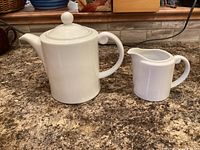 Royal Doulton white porcelain teapot with lid beside matching creamer on countertop