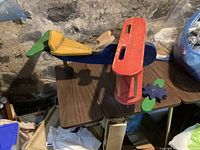 Side view of wooden biplane toy on table, missing wheel and detached propeller visible