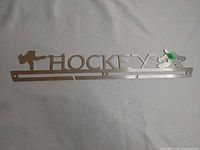 Full view of brushed metal hockey medal hanger showing word "HOCKEY," silhouettes and medal slots