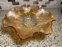 Oblique view of ruffled marigold carnival glass bowl showing holly pattern and iridescence