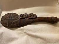 Full view of carved wooden club, showing flattened patterned head and handle
