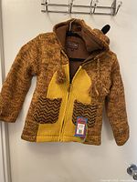 Front view of Kyber children’s knit sweater showing zipper, pockets, tassels, hangtag