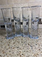 Four identical clear shot glasses standing upright showing swirl detail