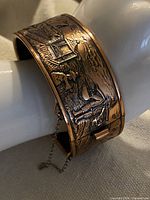 Full view of copper hinged bangle on display arm showing embossed scene and clasp side