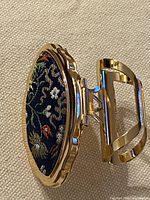 Lipstick holder standing open showing gold-tone metal, hinge and floral fabric inlay
