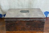 Closed rectangular silver-plated box showing monogram on lid and overall patina