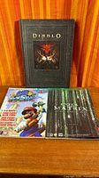 Three gaming books laid out: Diablo art book, Super Mario Sunshine guide, Enter the Matrix guide