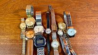 Group shot of all eleven wristwatches on wooden surface