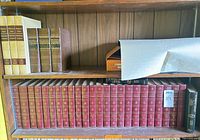 Shelf showing red Encyclopaedia Britannica volumes, brown replica volumes, additional items