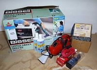 Group shot showing boxed Bissell cleaner, solution bottles, car vacuum, extension cord, car charger and tire chains