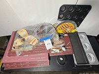 Lot overview showing Calphalon boxed bakeware, mini muffin pan, pie crust shields, giant cupcake pan, tartlet pans, seashell pan and rectangular tart pan