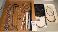Overview of box containing necklaces, bangles, watches, ring and boxed necklaces