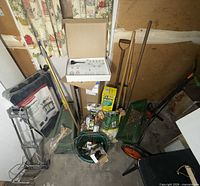 Grouped view of assorted garden tools, fertilizer bag, bucket, reel mower, string trimmer box and other items