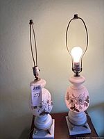 Full view of both matching lamp bases powered on, showing floral glass bodies, harps, and height