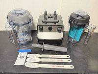 Front view of blender base, two pitchers, tamper and three spatulas