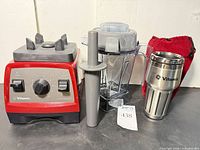 Front view of blender base, jar, tamper, travel cup and pouch