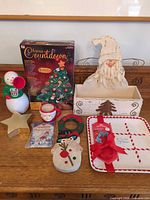 Group shot of entire lot showing advent calendar box, cookie plate, Santa planter, snowman figurine, Santa mug, wooden wreath and snowman ornament, gold star box