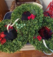 Artificial greenery wreaths with red accents in blue bin
