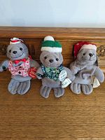 All three gray Coca-Cola Sealie plush seals standing side by side showing front view and accessories