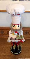 Front view of chef nutcracker showing hat, beard, tray with gingerbread house and hanging cookies
