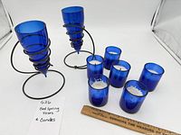 Full lot view showing two bed spring vases and six blue glass candles with ruler for scale