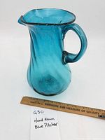 Full view of turquoise hand blown glass pitcher beside ruler