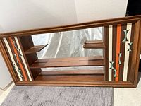 Front view of wooden curio shelf showing mirrored back, side patterned panels, interior shelves