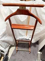 Full front view of wooden valet stand showing hanger, shelf, trouser bar