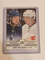 Front of Upper Deck Series One Checklist #199 card in plastic toploader showing Auston Matthews and Johnny Gaudreau imagery