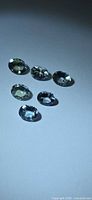 Six oval faceted blue-green gemstones on light background