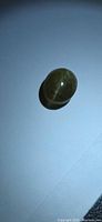 Top view of olive-green oval cabochon showing chatoyant line