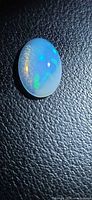 Oval cabochon opal showing blue, green play-of-colour on textured black background
