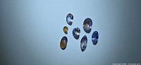 Seven faceted tanzanite stones laid out on light background