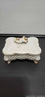 Angle view of closed trinket box showing quilted pattern and gilt finial