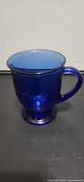 Side view of cobalt blue Starbucks etched glass mug showing handle and pedestal base