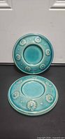 Front view of both turquoise ceramic candle saucers showing floral design and recessed center