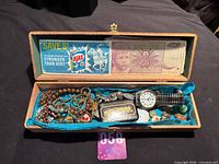 Open wooden box showing contents including watch, beads, knife, coupon, banknote