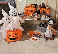 Overall view showing inflatable pumpkin with ghosts, numerous pumpkin pails, small tabletop items on table and freestanding ghost figure