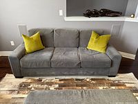 Front view of grey three-seat sofa with two green pillows
