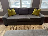 Front view of grey three-seat sofa with two green pillows