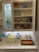 Open cabinet showing multiple plastic containers and white plastic baskets on countertop