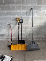 Four long-handled yard and winter tools leaning against concrete block wall