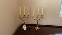 Pair of brass Baldwin five-arm candelabras with taper candles and brass-handled copper snuffer on surface